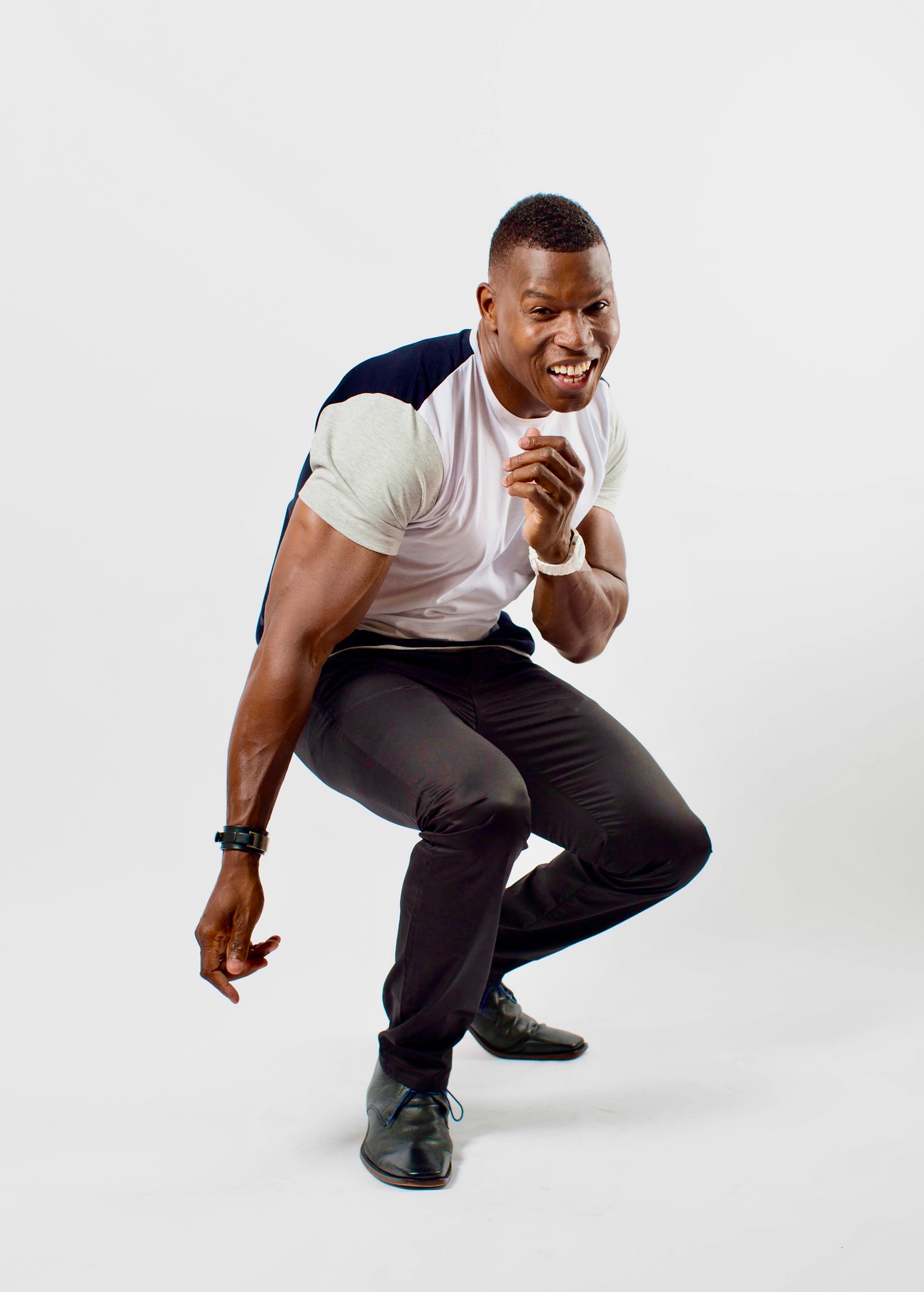 Lawrence Beamen crouching playfully mid-laugh on a white backdrop