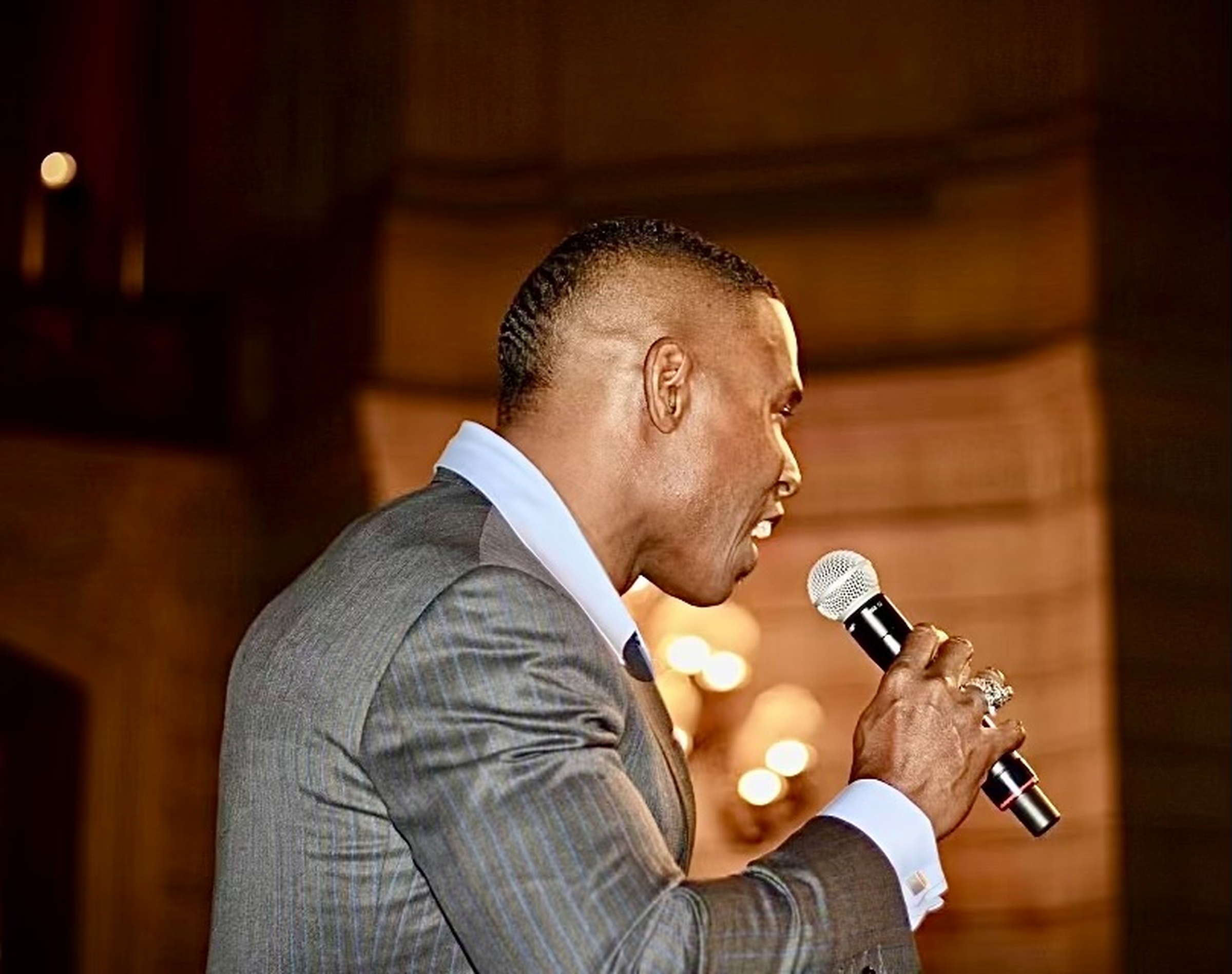 Lawrence Beamen singing on stage in a pinstripe suit under warm light