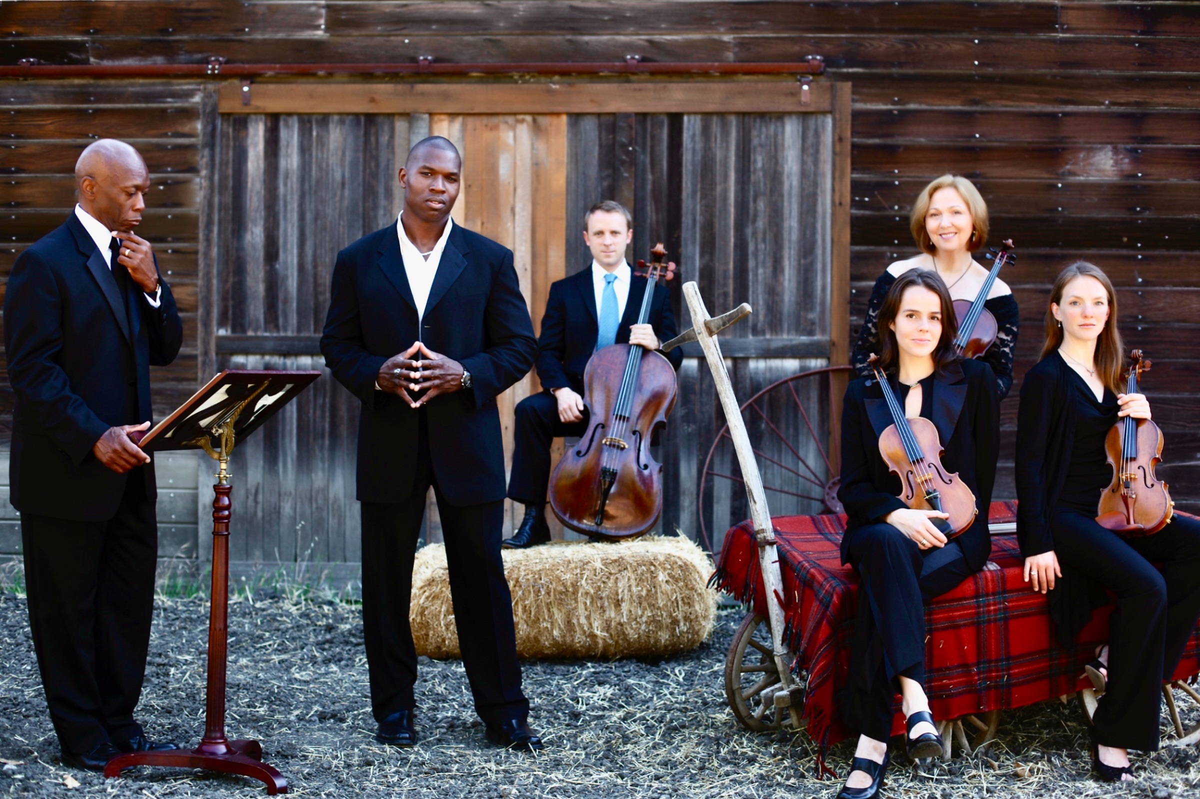 Lawrence Beamen standing with a string quartet outside a weathered barn