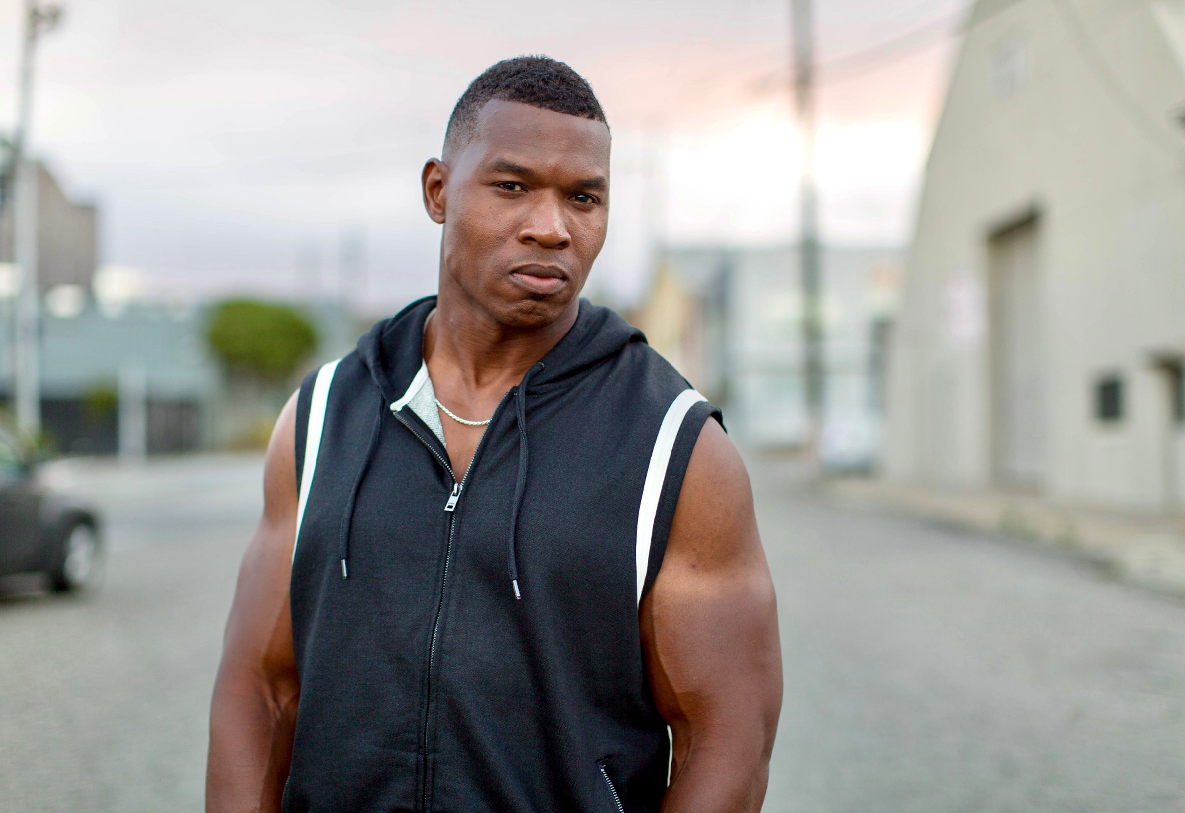 Lawrence Beamen photographed on a street at dusk in a sleeveless hoodie