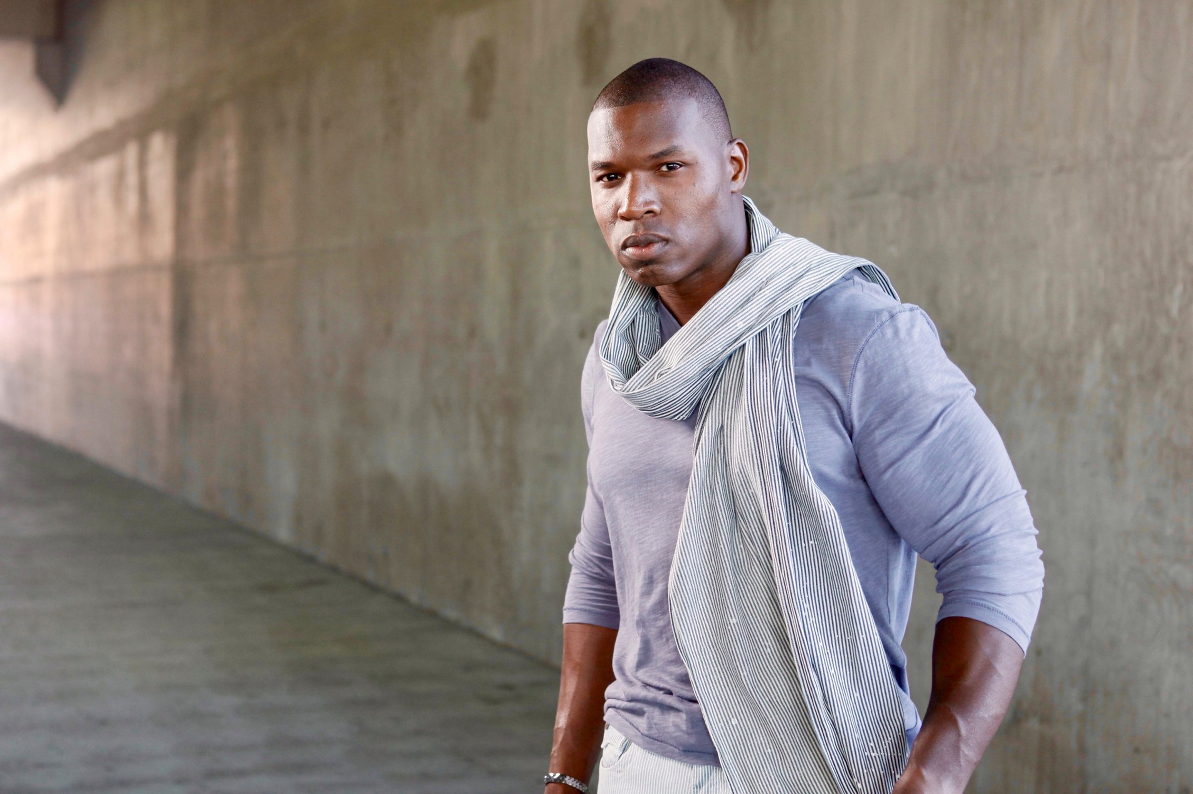 Lawrence Beamen in a scarf and grey top against a concrete underpass wall