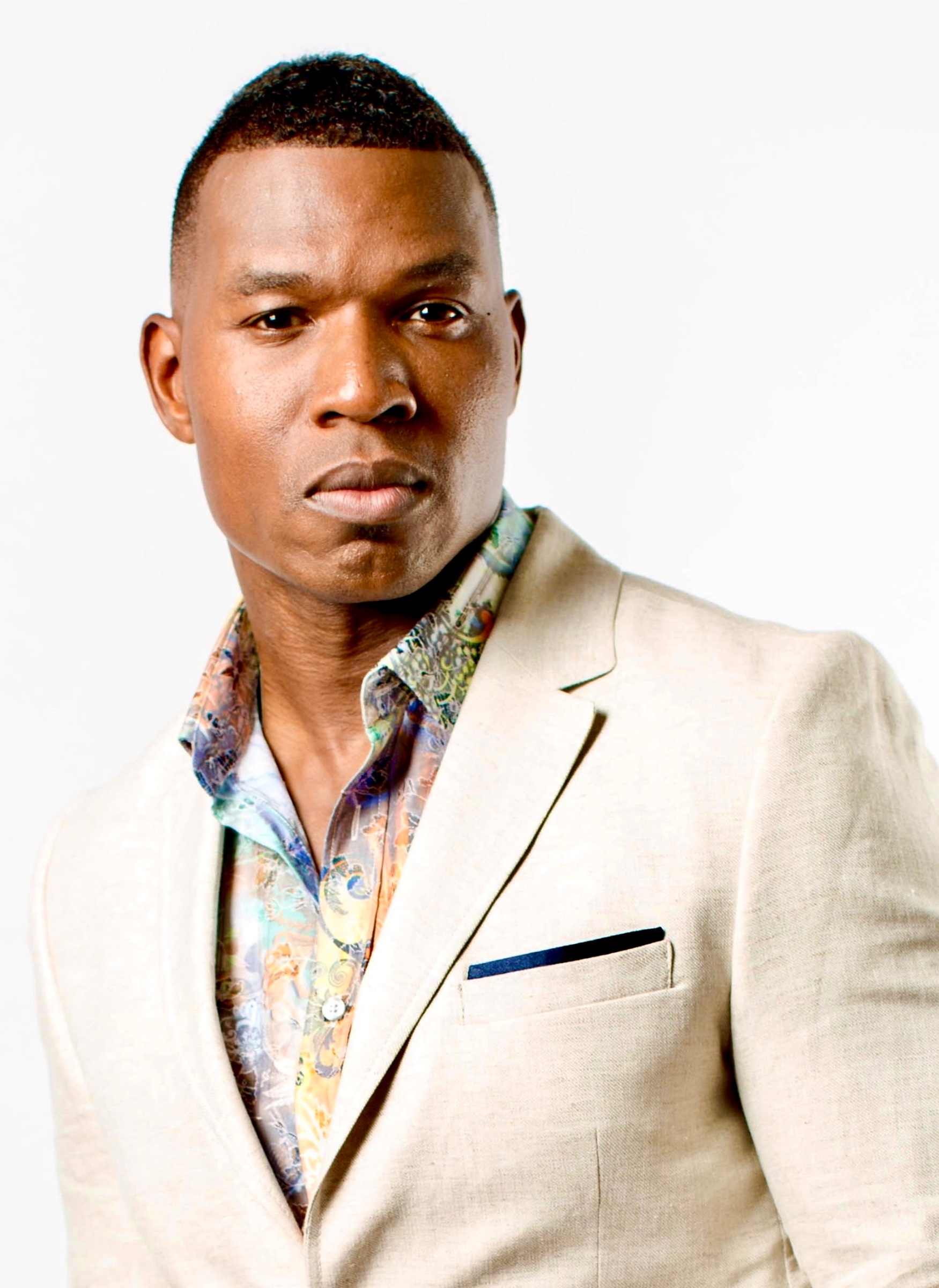Lawrence Beamen in a cream linen suit and patterned shirt on white