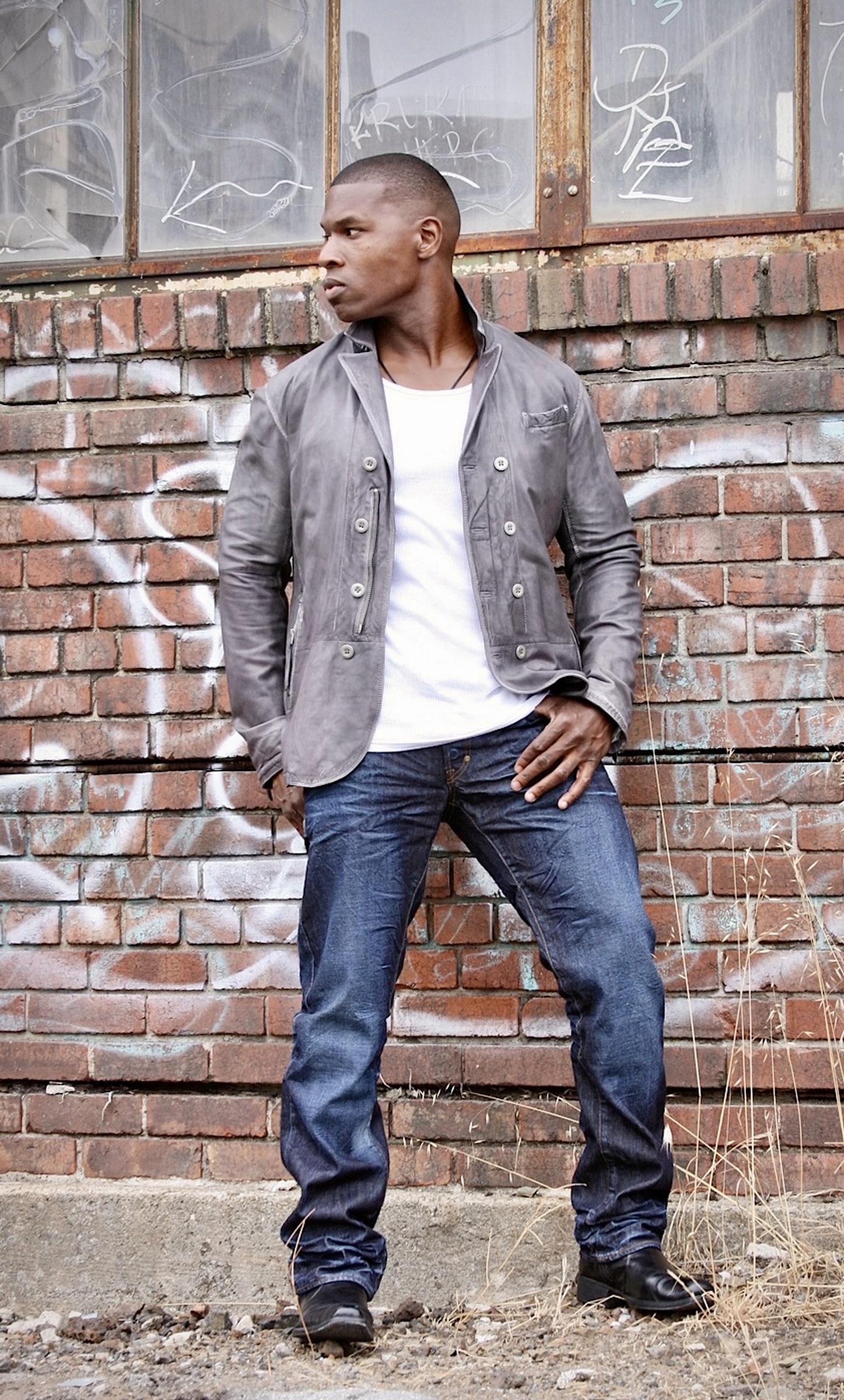 Lawrence Beamen in a grey jacket and jeans against a graffiti brick wall